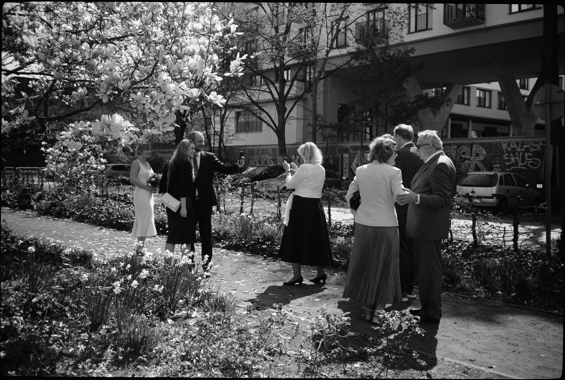 Guests in a garden among blossoming trees, in black and white, Irena & Peter wedding in Berlin