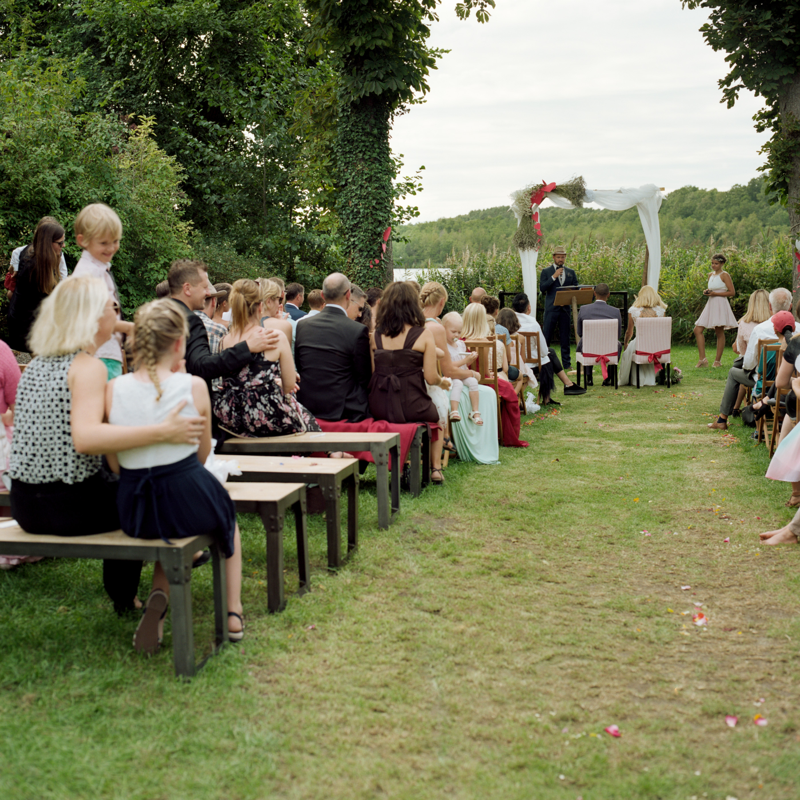 Guests seated on benches for the lakeside garden ceremony, Linda & Thomas wedding in Berlin