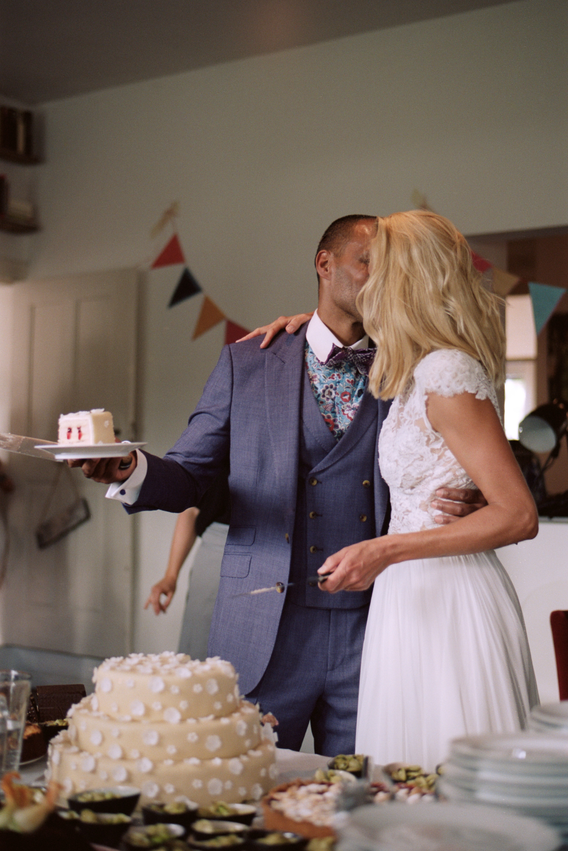The couple beside their cake under paper bunting indoors, Linda & Thomas wedding in Berlin