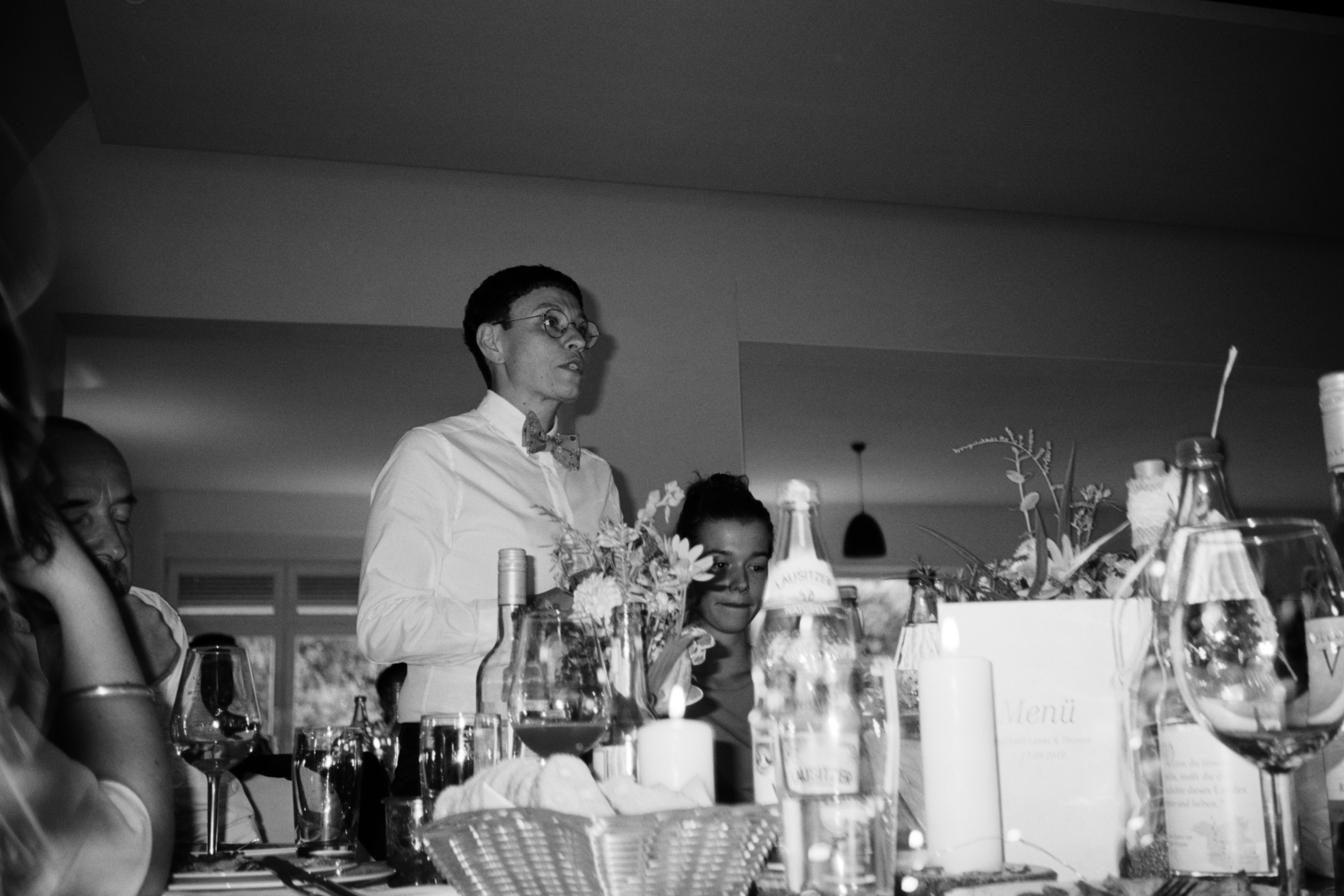 A guest among the wine glasses at the long dinner table, black and white, Linda & Thomas wedding in Berlin