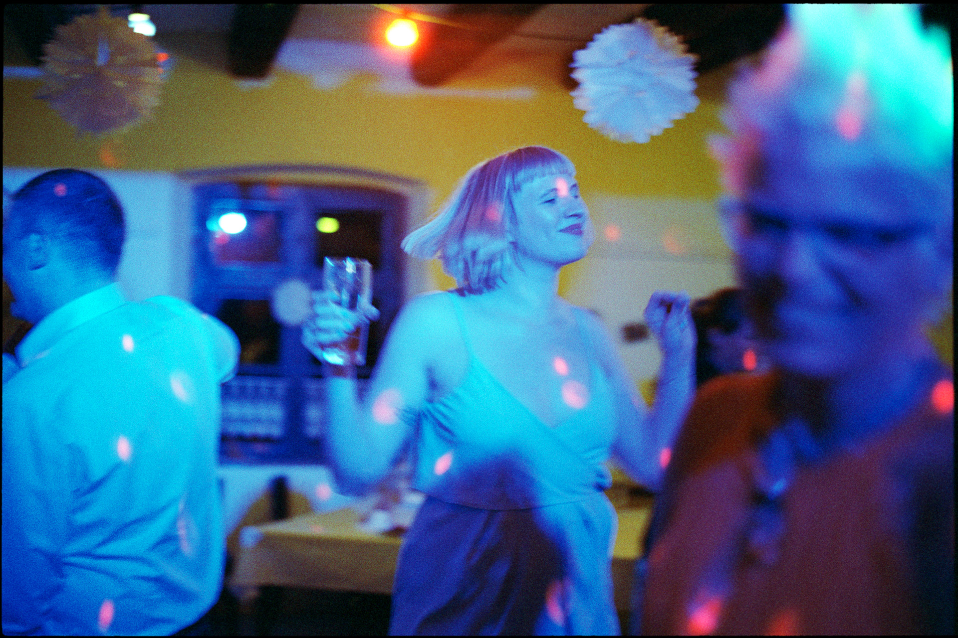 A guest dancing under blue light, drink in hand, Maike & Daniel wedding in Brandenburg
