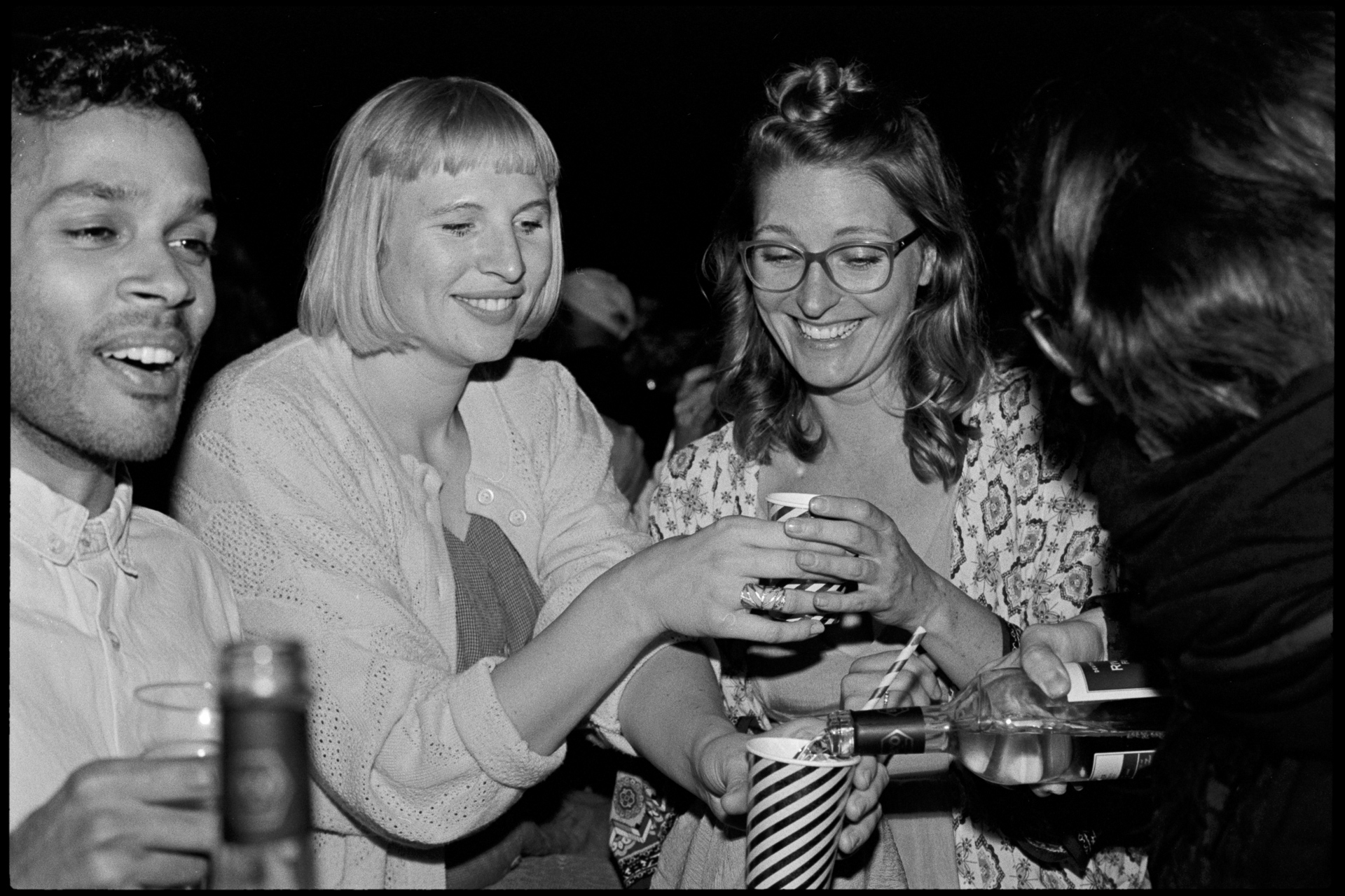 Guests laughing together with drinks, in black and white, Maike & Daniel wedding in Brandenburg