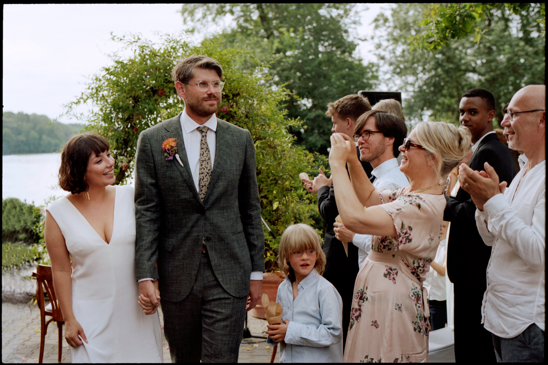 The couple walking through applauding guests by the lake, Suelyn & Pascal wedding in Groß Glienicke, Potsdam