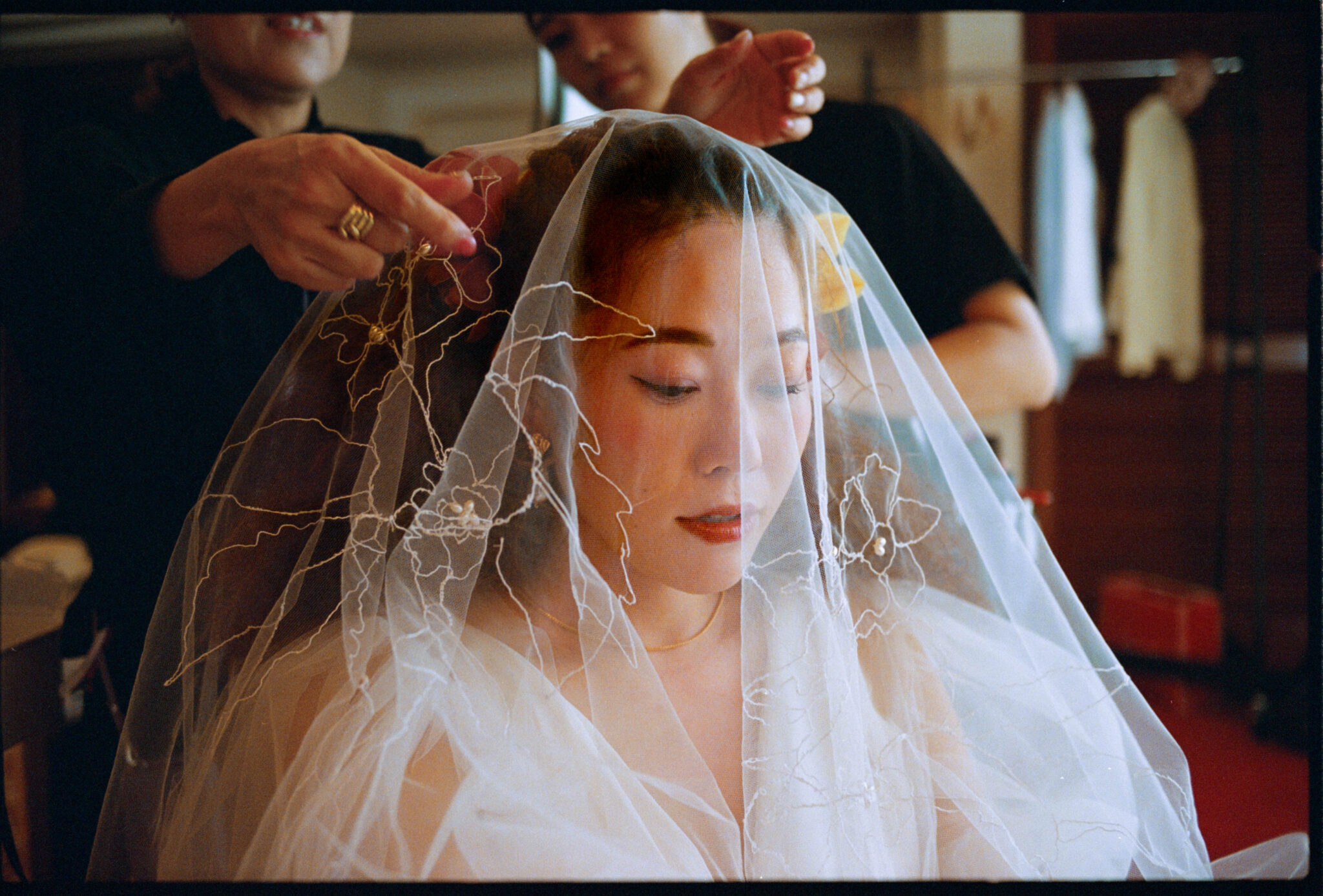 Embroidered veil being arranged over the bride's face while she gets ready, analogue film photograph by Martina Manz