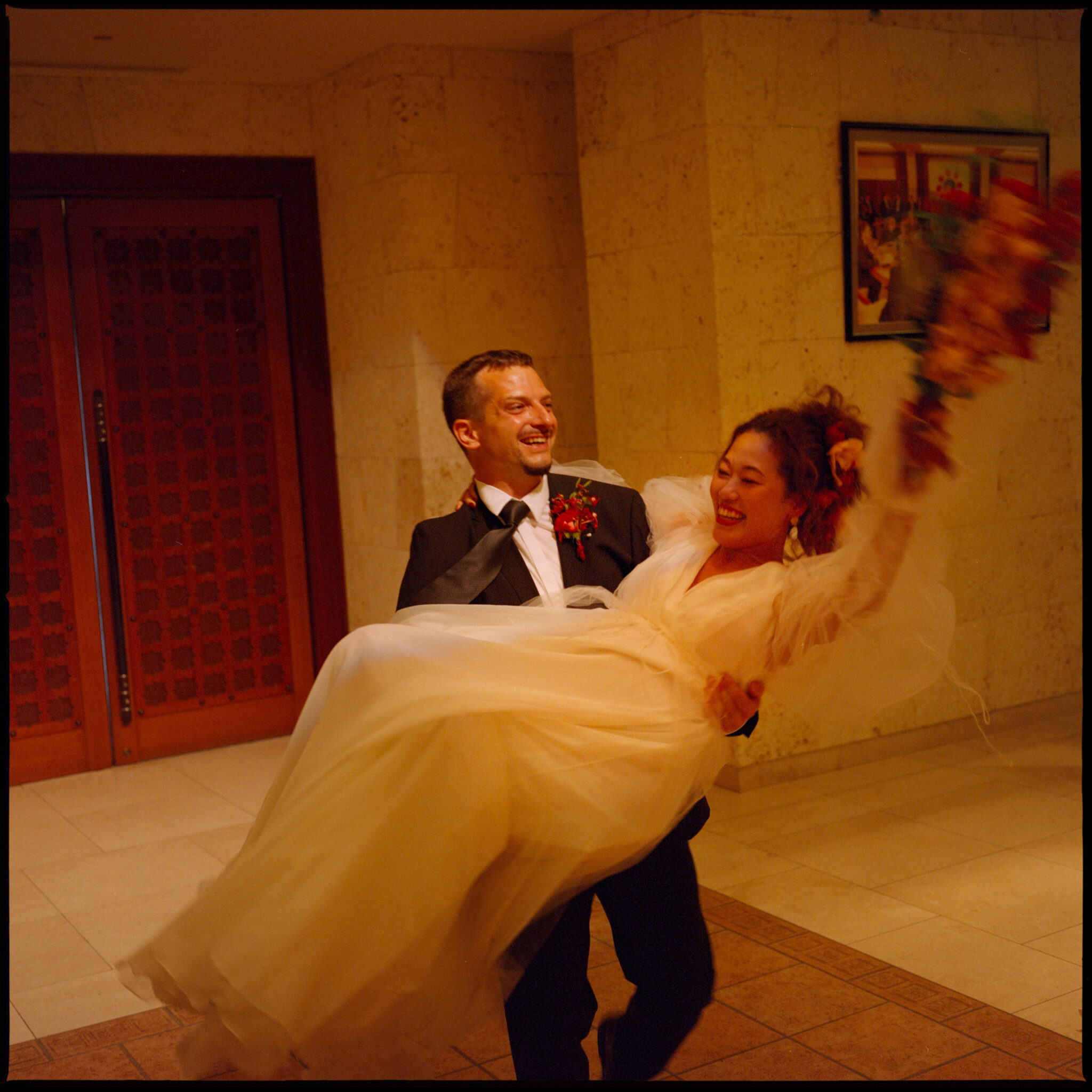 The groom carrying the bride, arms thrown up, Sugano & Jonas wedding in Okinawa