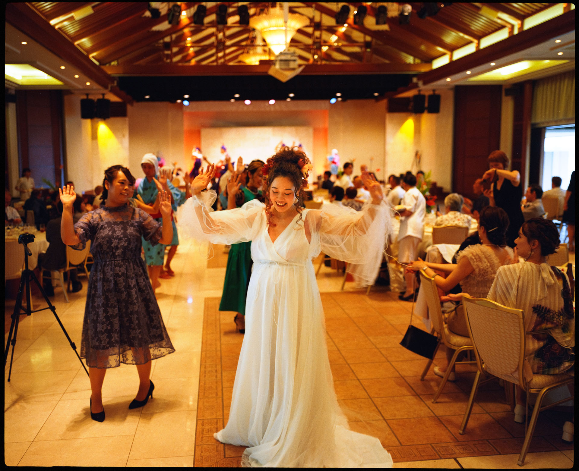 Bride entering the reception hall with open arms while guests cheer, analogue film photograph