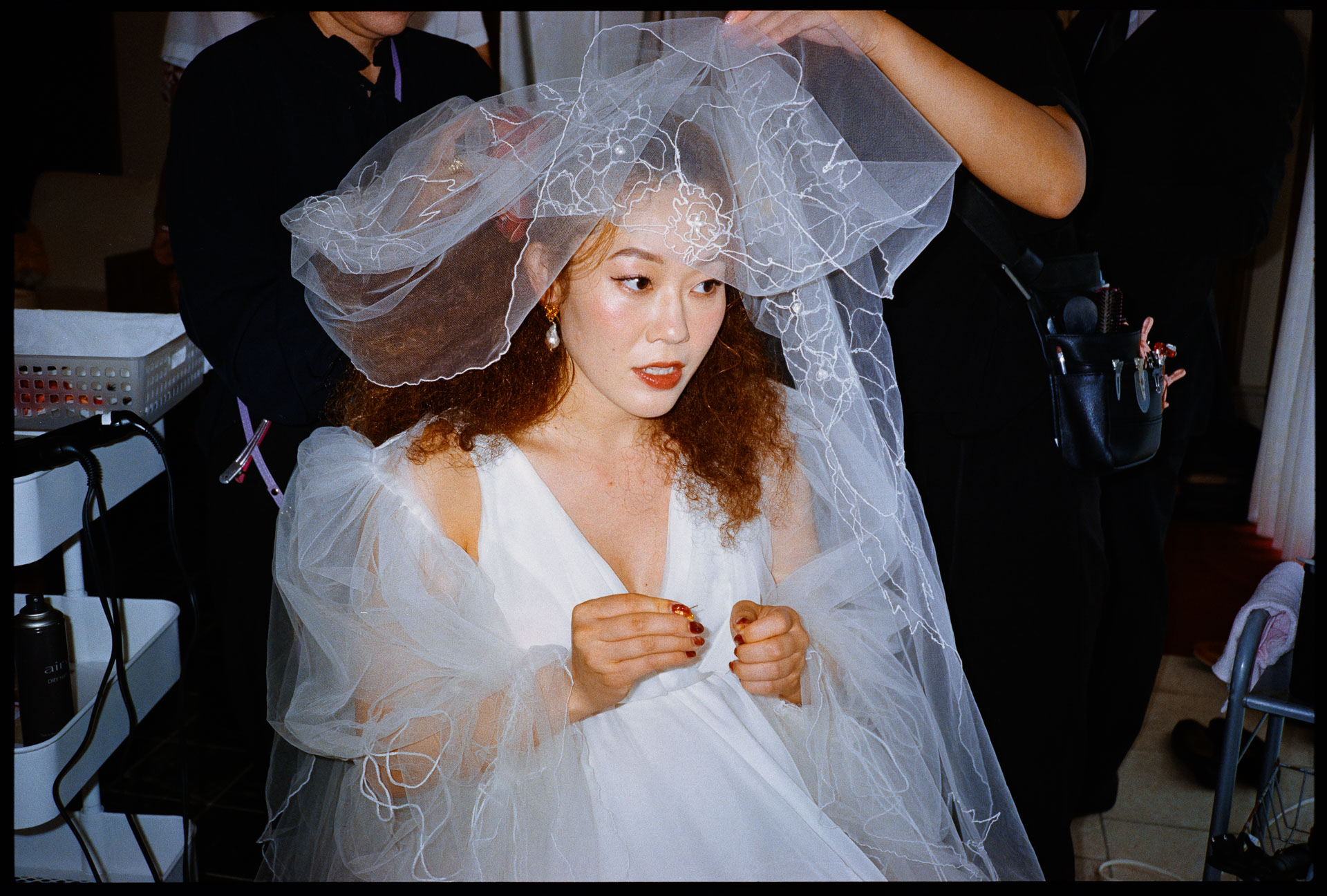 Bride glancing to the side as her embroidered veil is arranged while getting ready, analogue film photograph