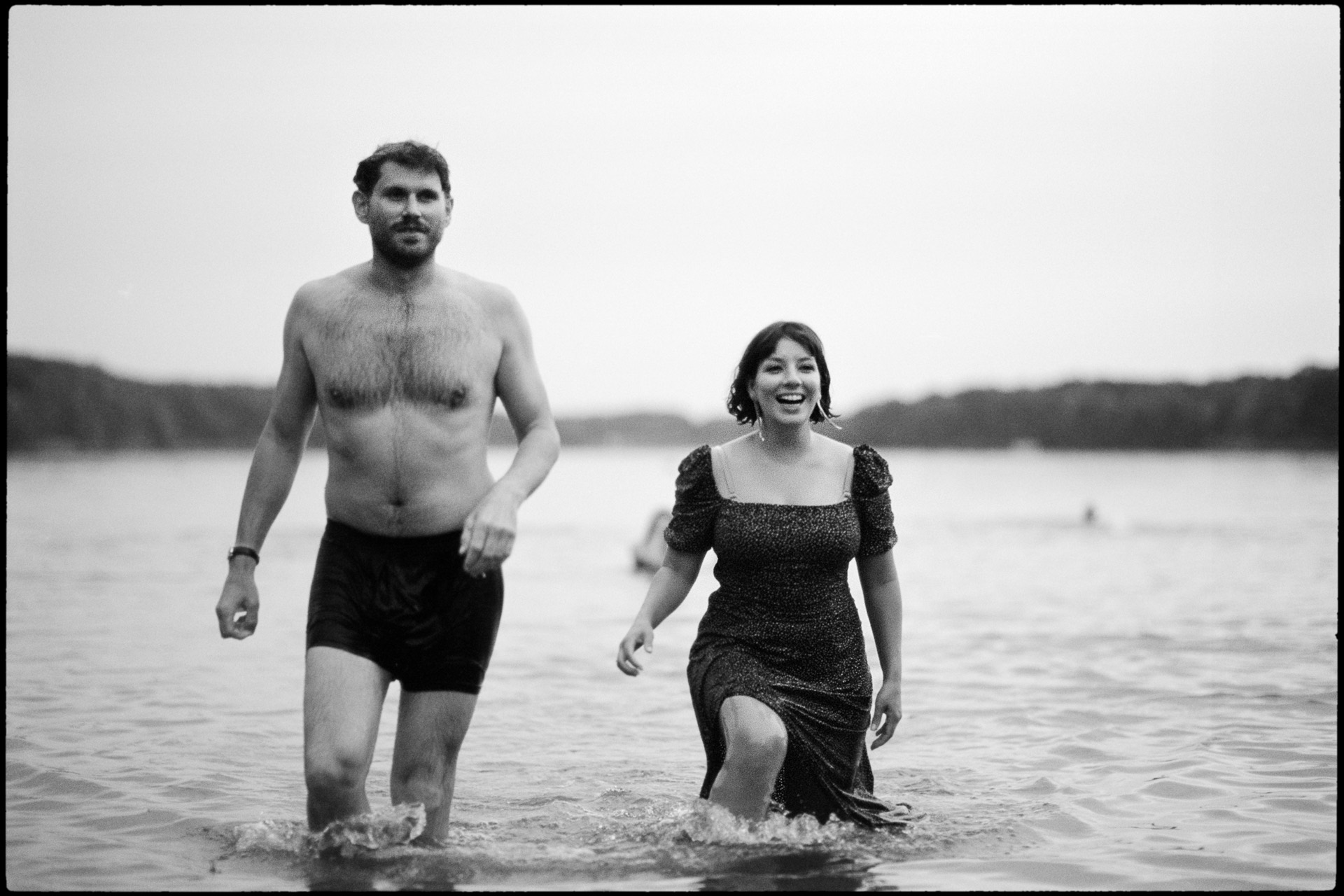 Couple laughing as they wade out of a lake, black and white film photograph