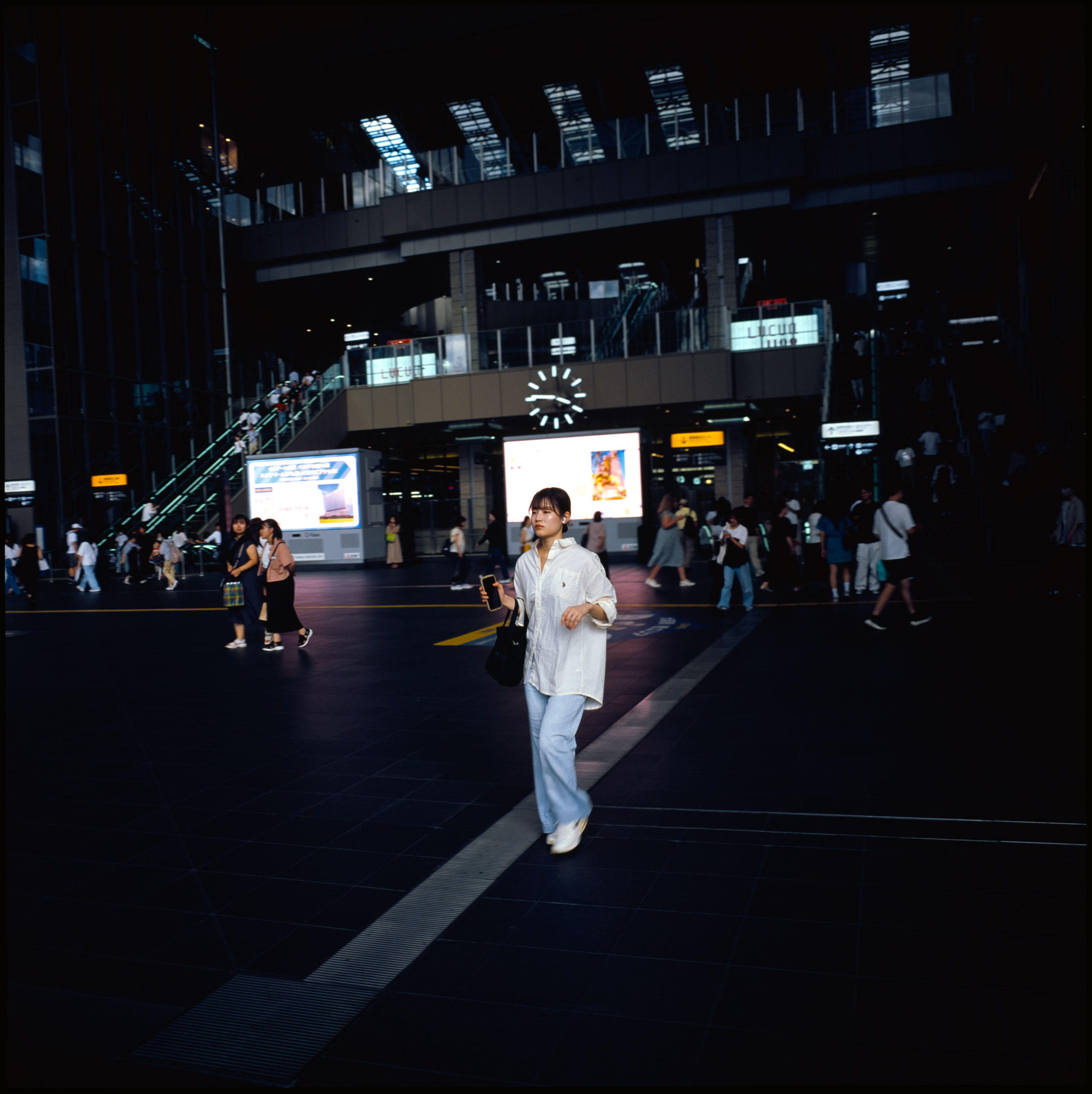 Woman with a phone crossing the dim forecourt of Osaka Station beneath the illuminated clock