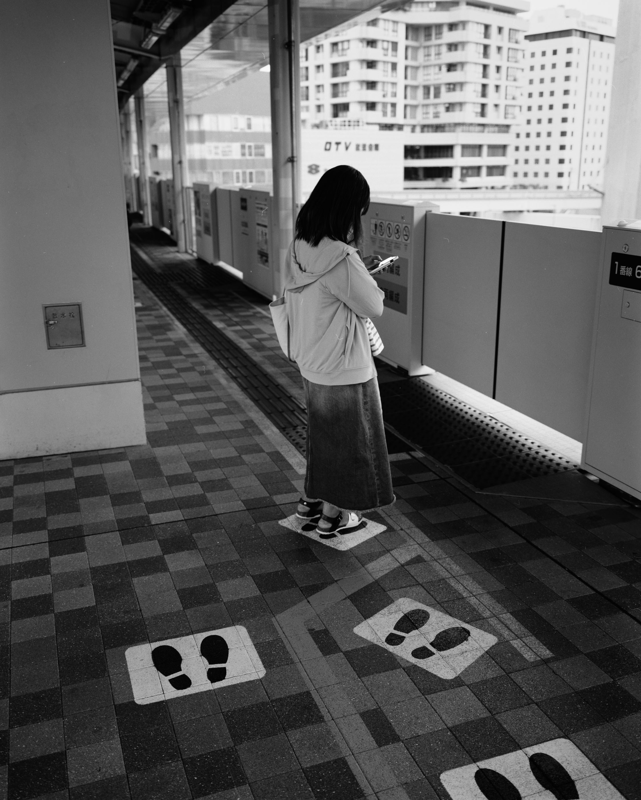 Woman looking at her phone on an elevated platform, standing on painted queue footprints
