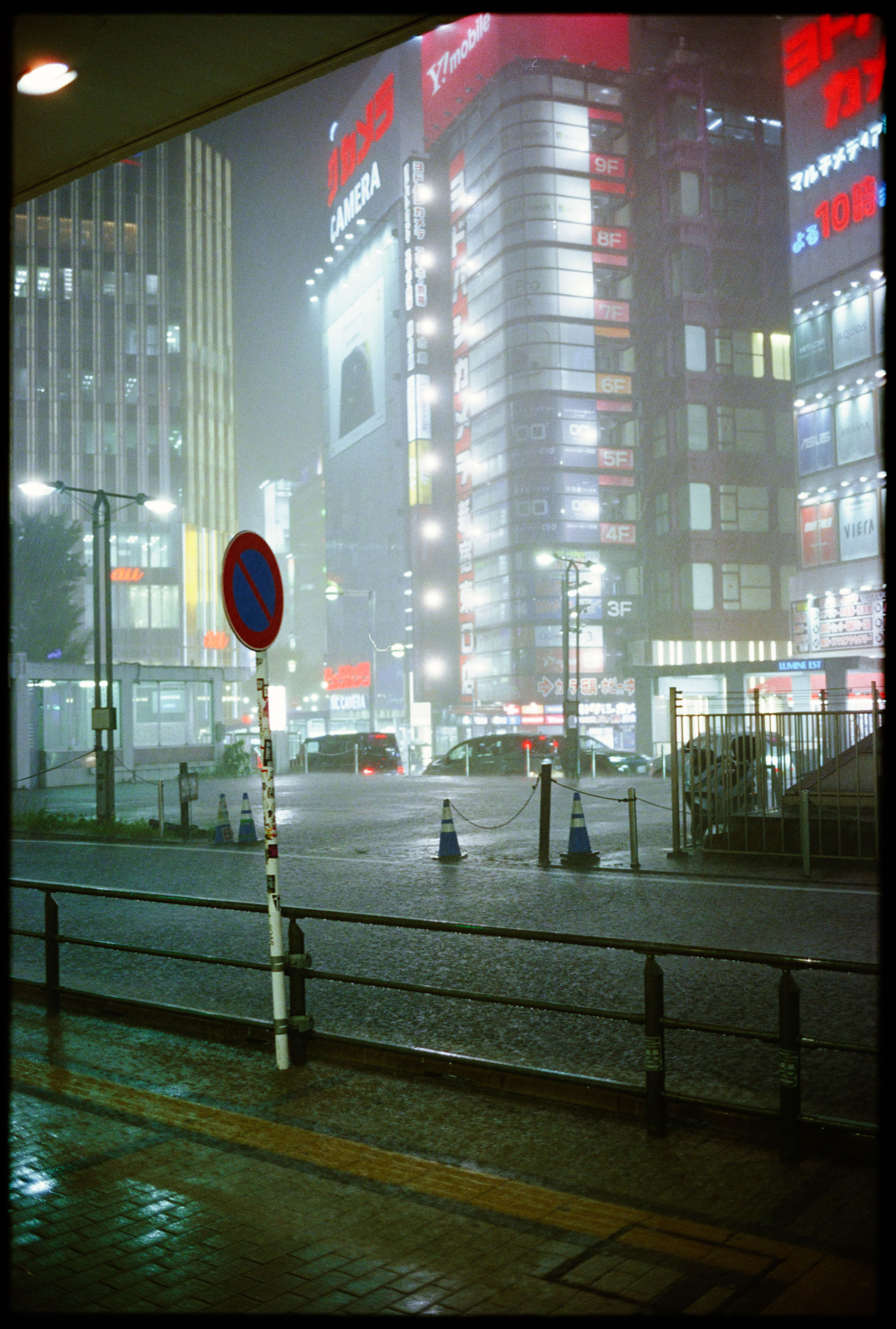 Night rain pouring on the square at Shinjuku Station's east exit, electronics signs glowing through the mist