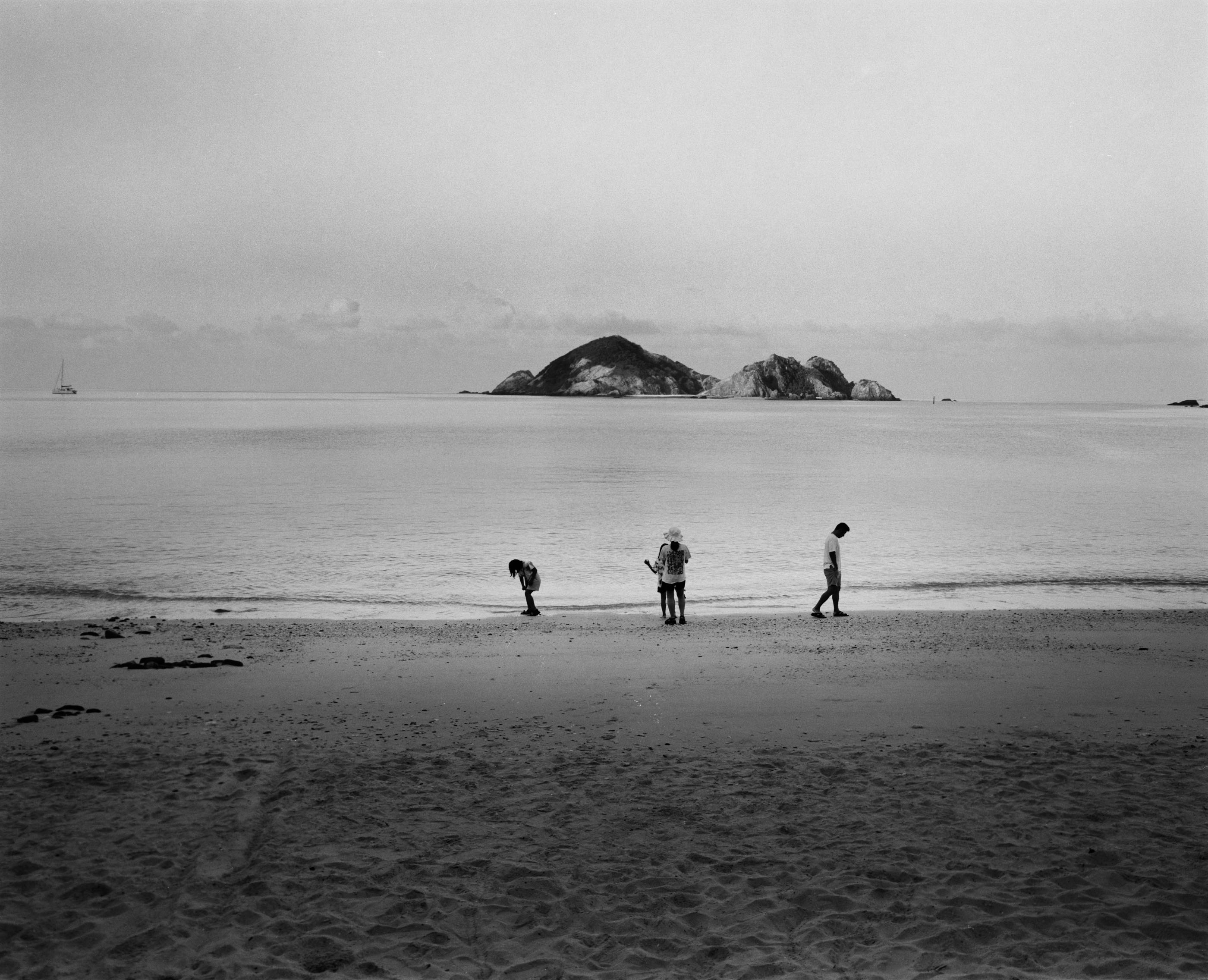 Family of three searching the shoreline at dusk, two rocky islets across the still water