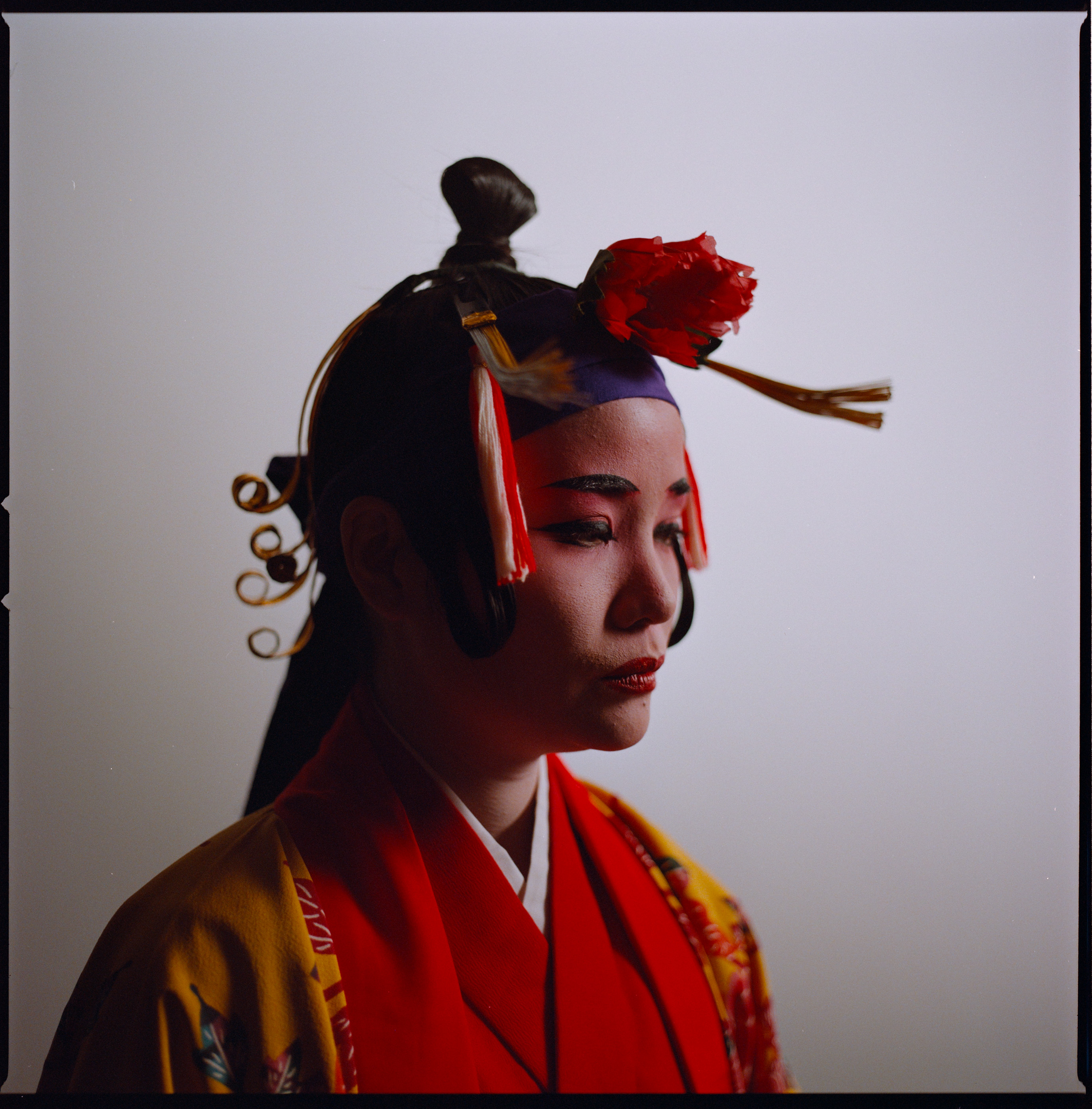 A performer in profile in a red and gold Ryukyuan costume with a flower headpiece, analogue film portrait by Martina Manz, Berlin
