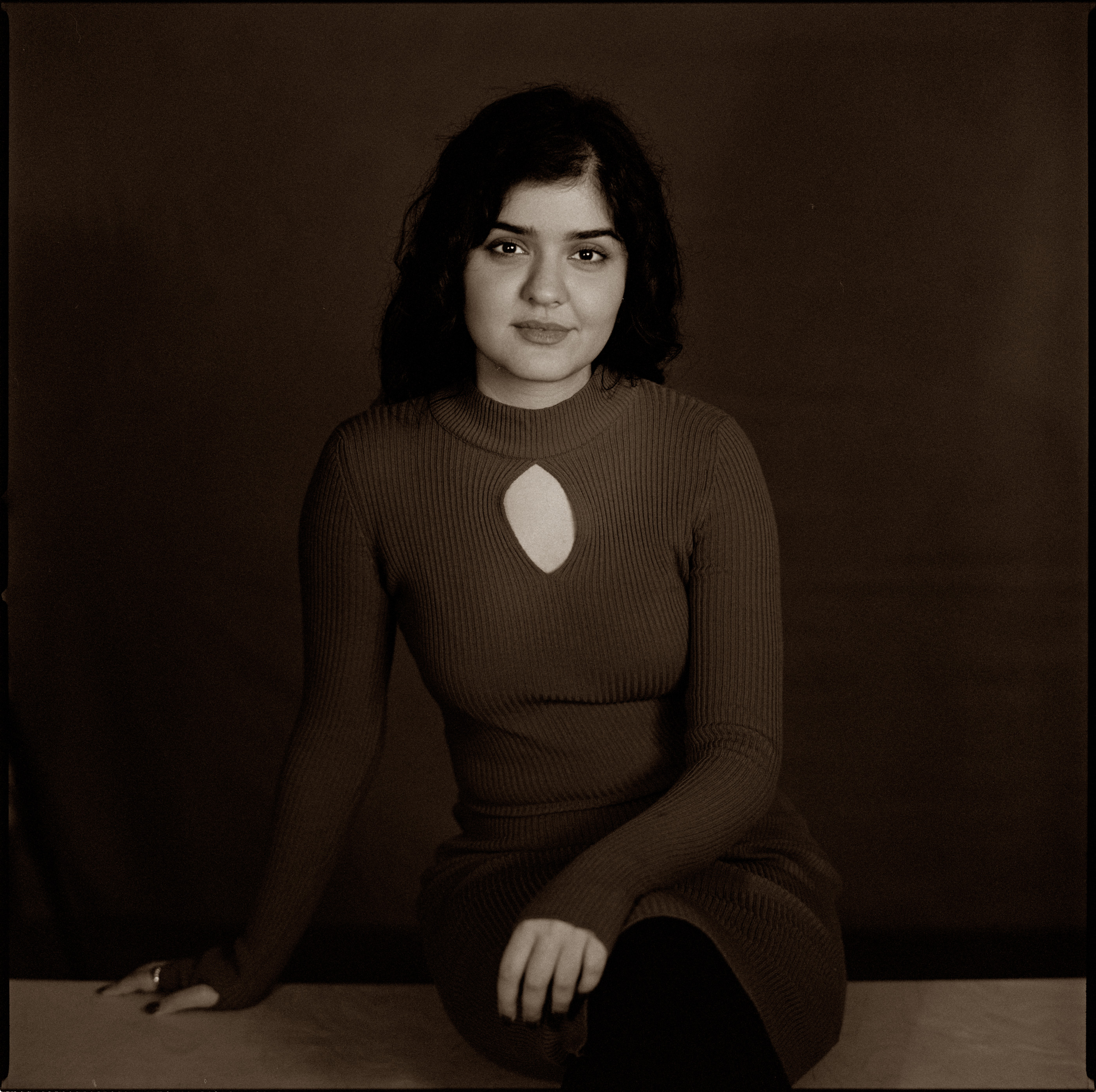 A woman seated in a brown ribbed dress in warm tones, analogue film portrait by Martina Manz, Berlin