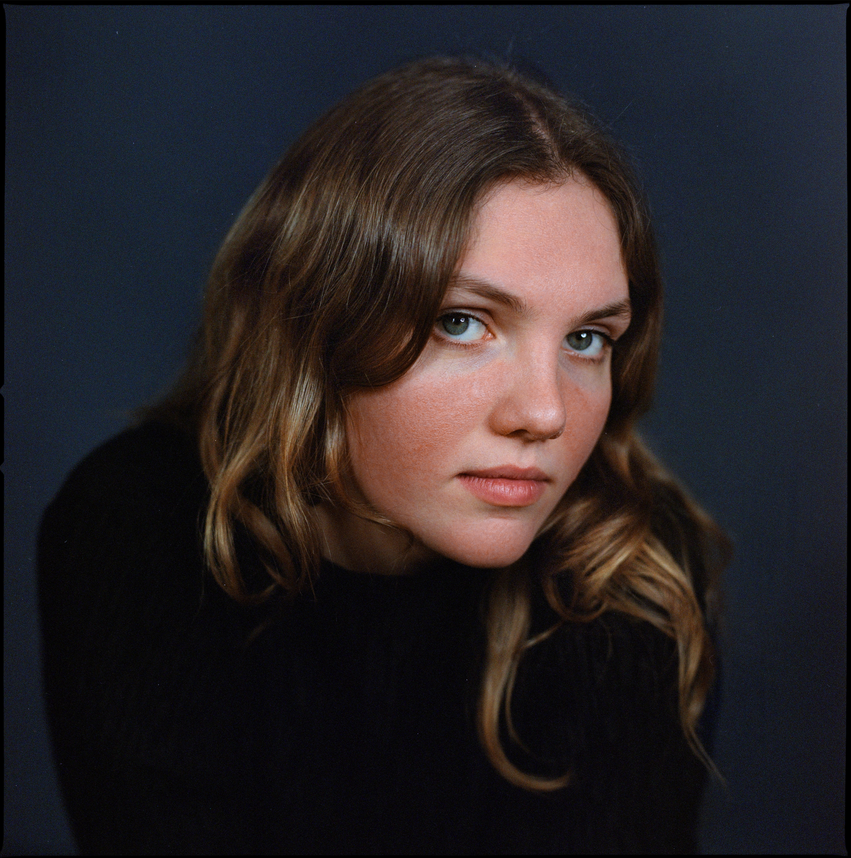 A woman with wavy hair against a blue-grey backdrop, analogue film portrait by Martina Manz, Berlin