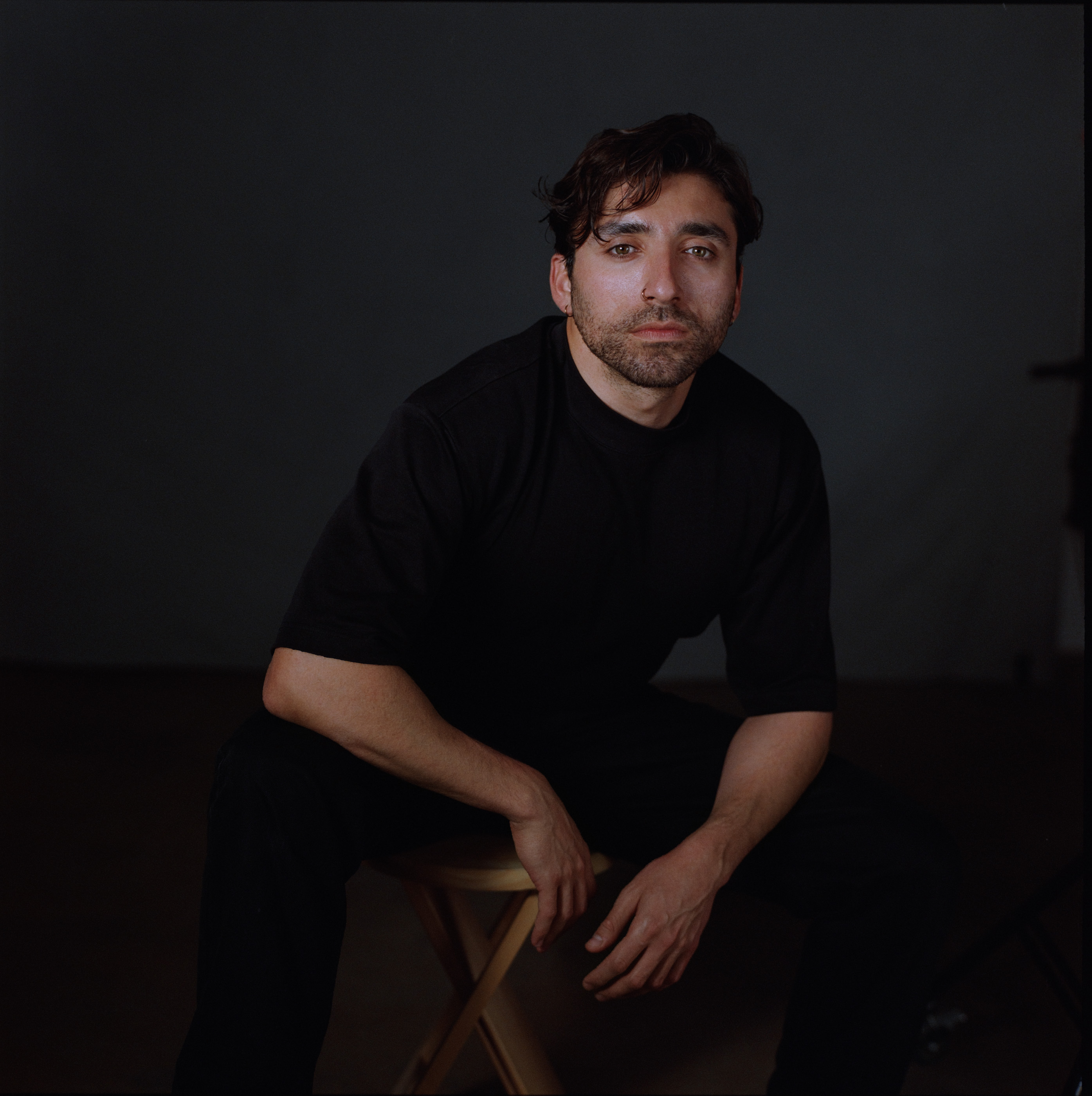 A man dressed in black seated and looking towards the camera, analogue film portrait by Martina Manz, Berlin