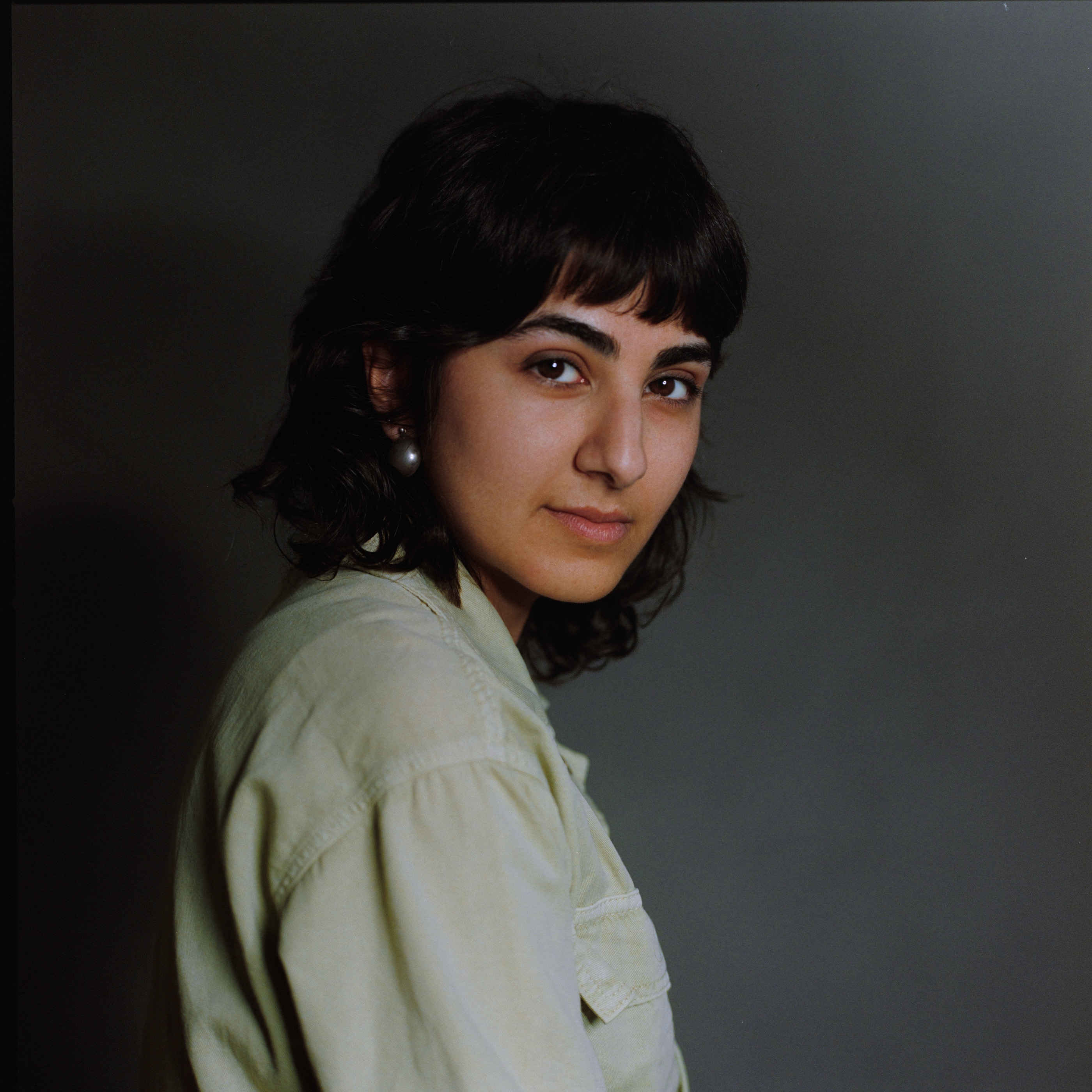 A woman in a pale green shirt turning towards the camera, analogue film portrait by Martina Manz, Berlin