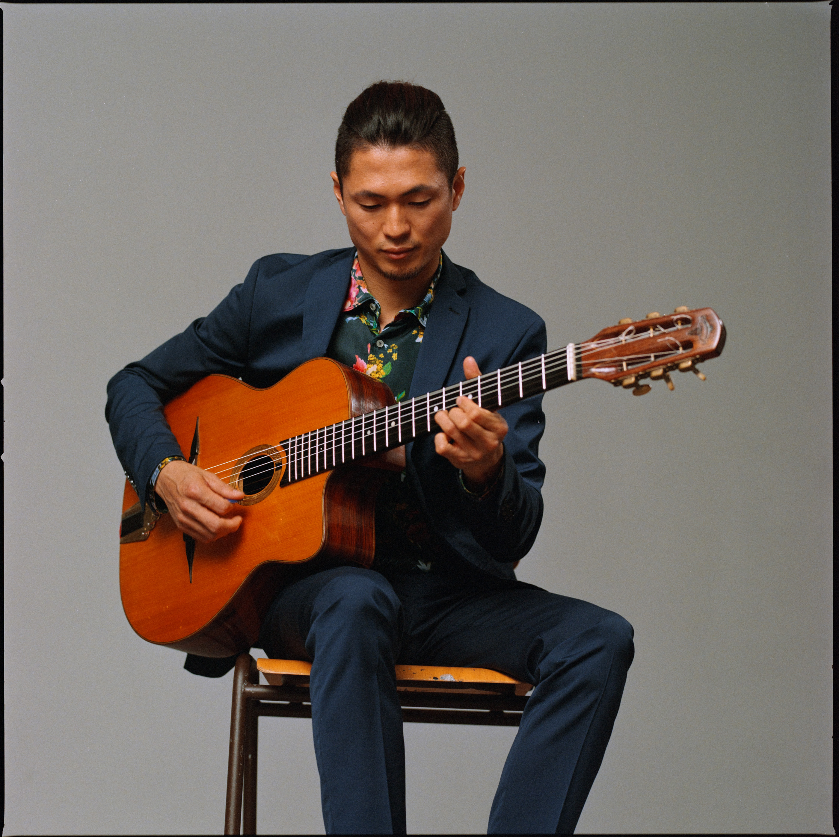 A musician seated playing an acoustic guitar in a blue suit, analogue film portrait by Martina Manz, Berlin