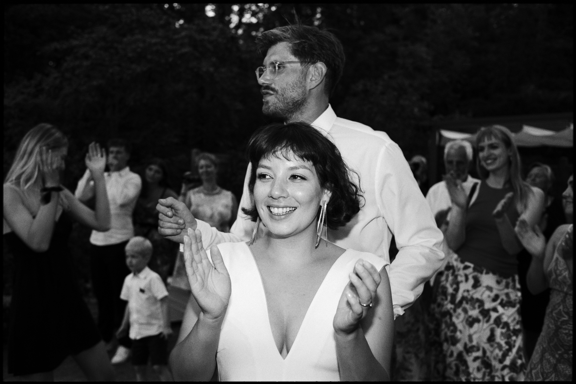 Bride dancing and clapping among cheering guests at a wedding reception, analogue film photograph by Martina Manz